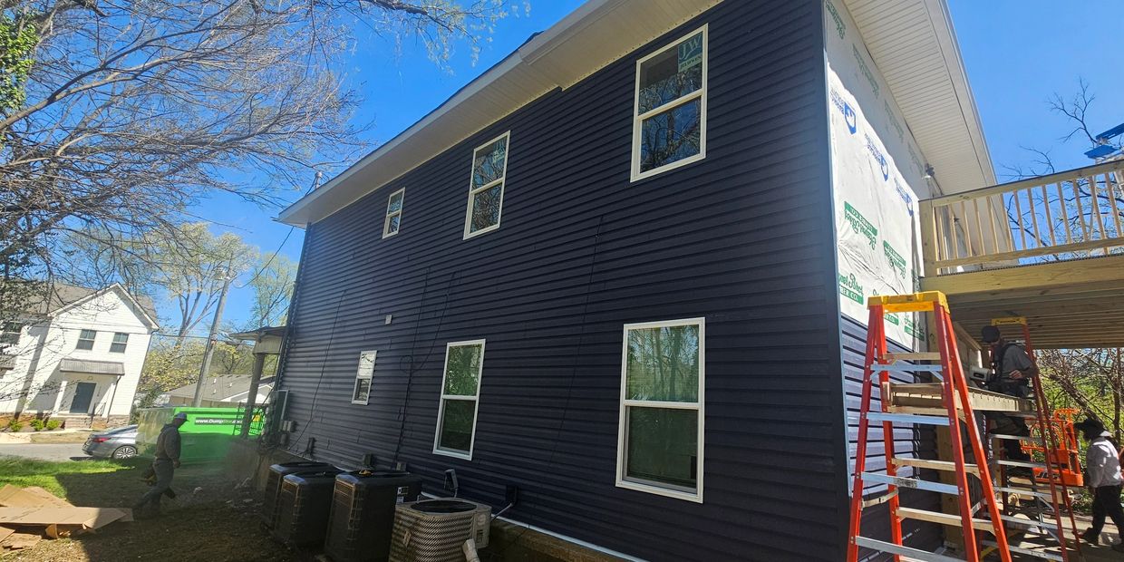 Workers installing siding on a two-story house under clear blue skies.