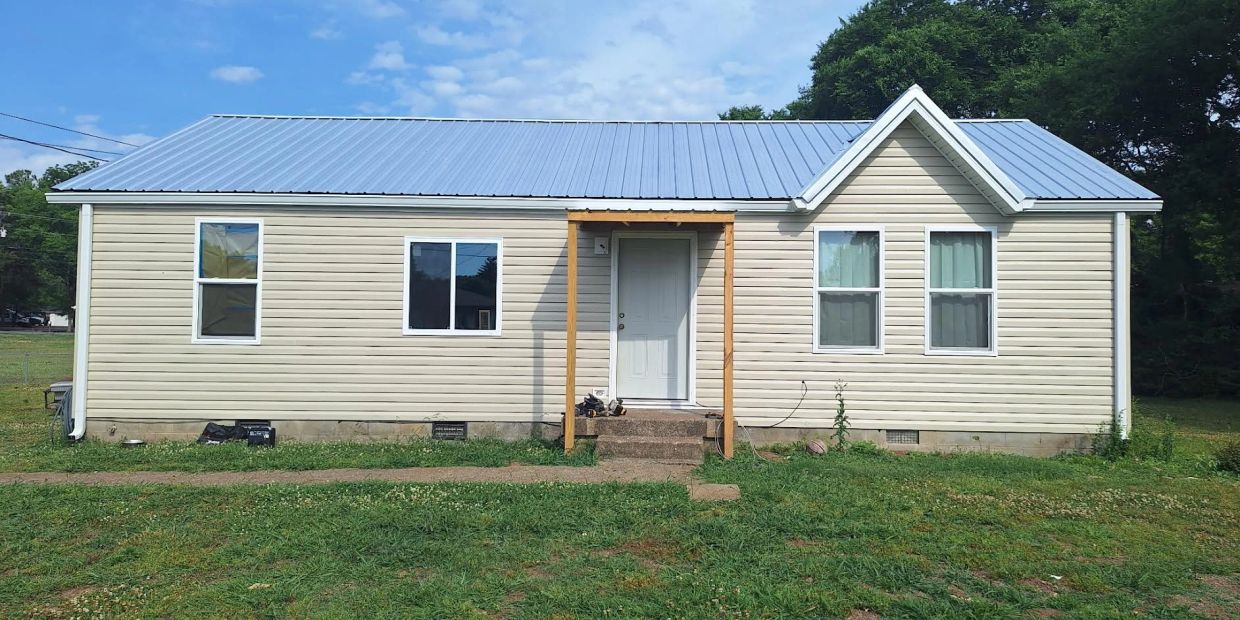 Single-story beige house with a blue metal roof and a small wooden porch.