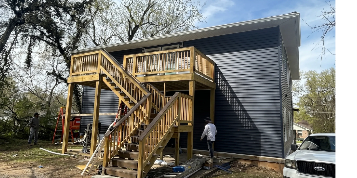 Newly constructed wooden staircase and deck attached to a blue house with workers around.