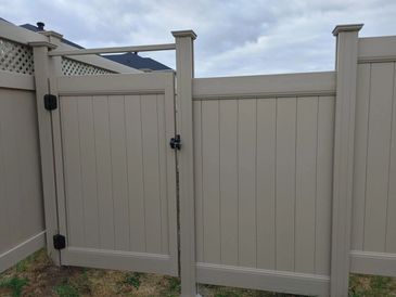 A beige vinyl privacy fence with a latched double gate under a cloudy sky.