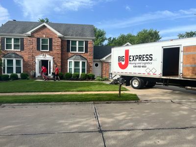 A moving truck parked outside a two-story brick house with people unloading.