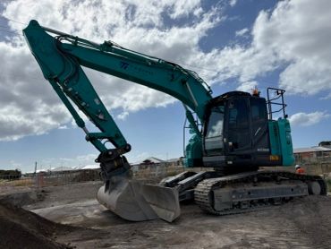 A teal excavator on a construction site under a partly cloudy sky.