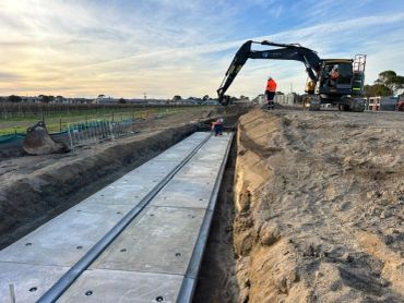 Excavator and workers installing concrete panels at a construction site.