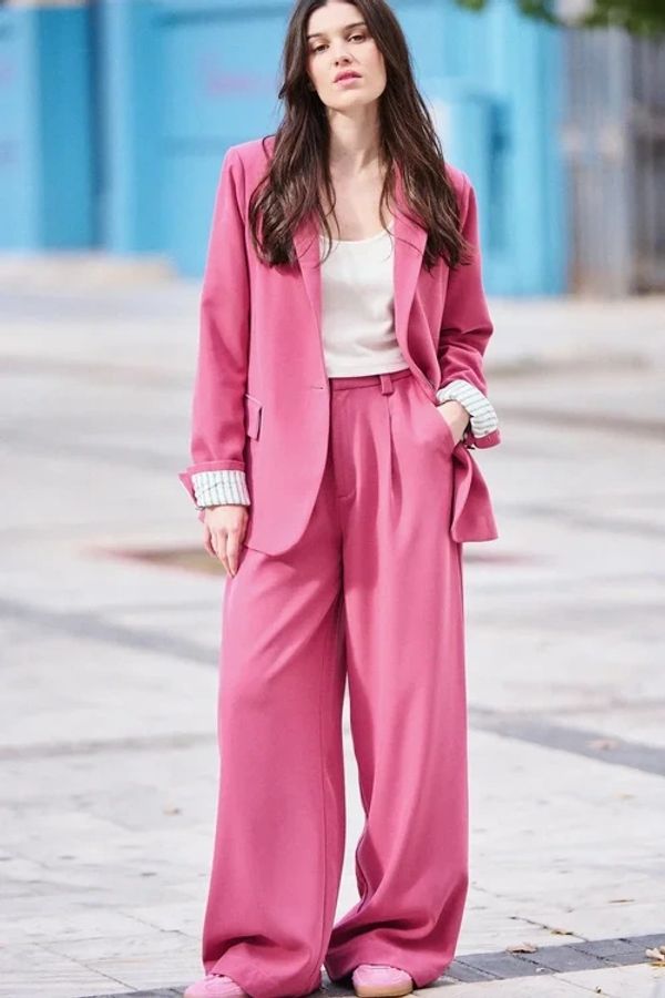 Woman in a stylish pink suit with wide-leg pants and a white top.