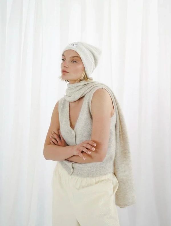 Woman in beige winter outfit with hat, scarf, and vest.