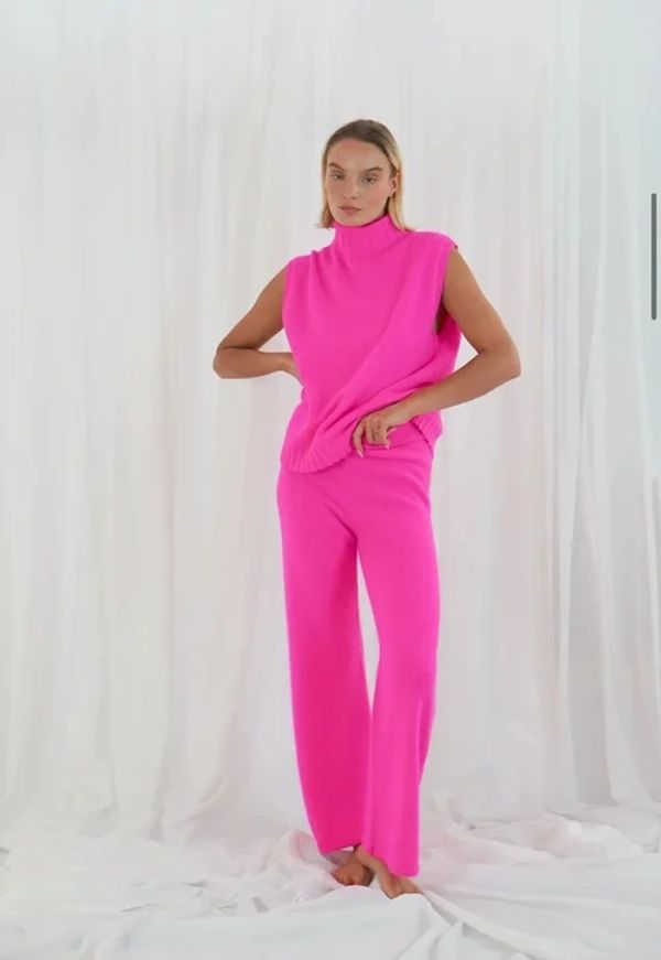 Woman in vibrant pink sleeveless top and pants posing barefoot.