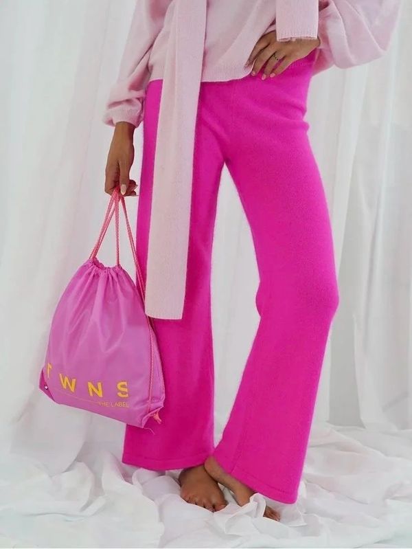 Person wearing bright pink pants and a light pink sweater, holding a pink drawstring bag.