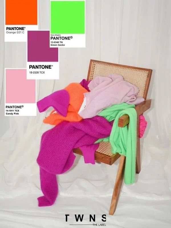 Colorful sweaters draped over a wooden chair with Pantone color swatches.