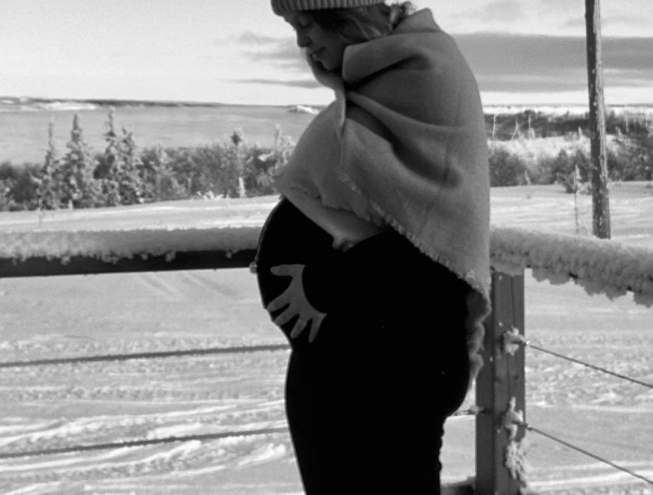 Pregnant woman wrapped in a shawl standing outside in a snowy landscape.