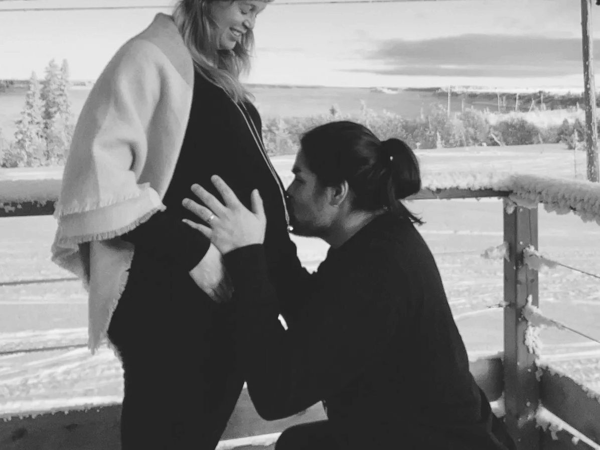 Man kisses pregnant woman's belly outdoors in winter.