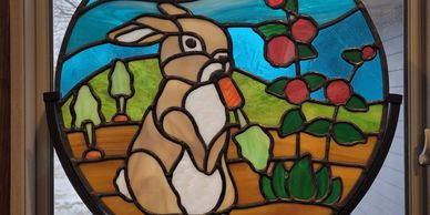 A stained glass panel depicting a rabbit eating a carrot in a garden.