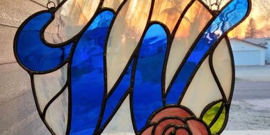 A stained glass decoration with a blue letter 'W' and a red rose.