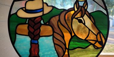 Stained glass art of a woman with a horse in a nature scene.