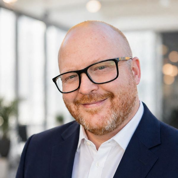 Smiling man with glasses in a suit jacket and white shirt.