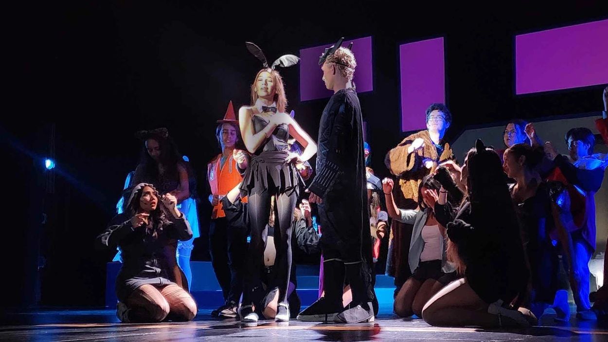 Group in costumes performing on stage with spotlight.