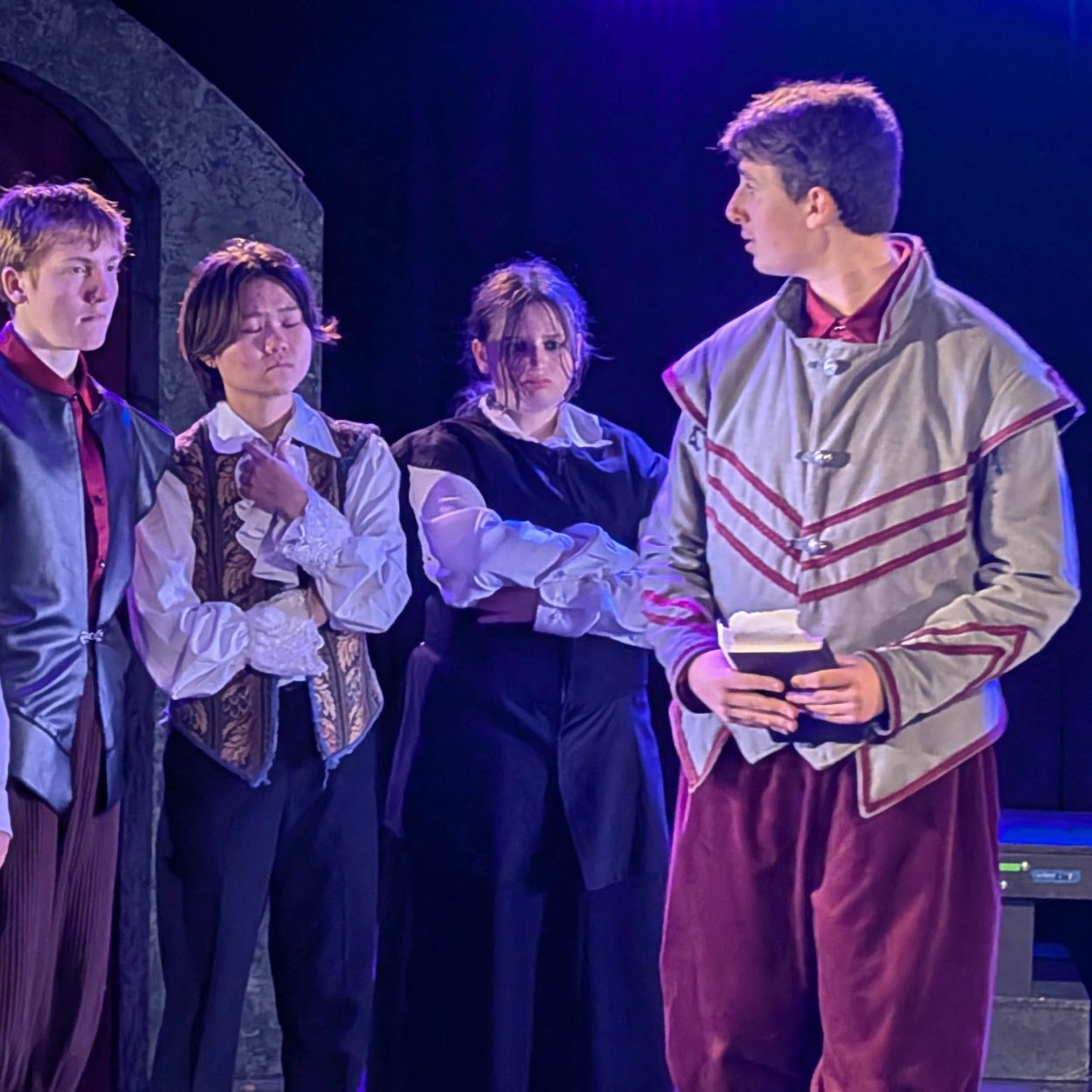 Actors in period costumes on stage during a play.