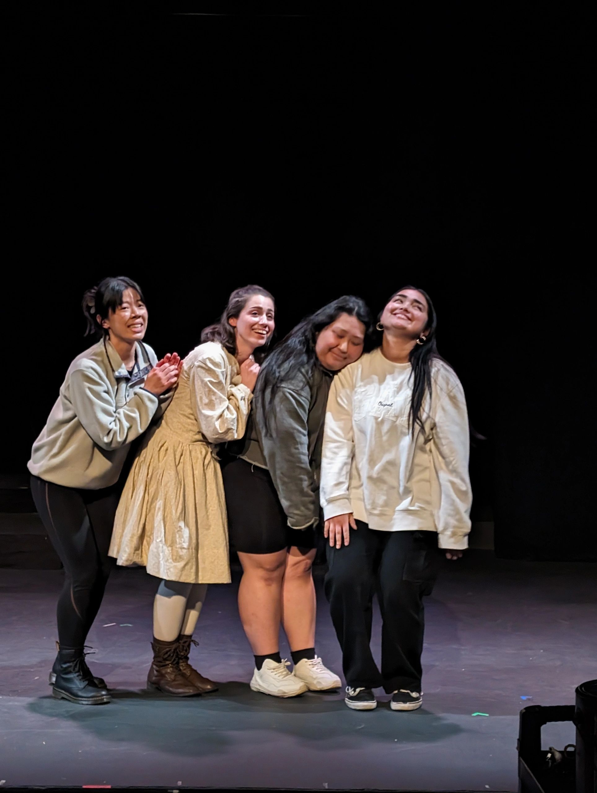Four women posing happily on stage with a dark background.