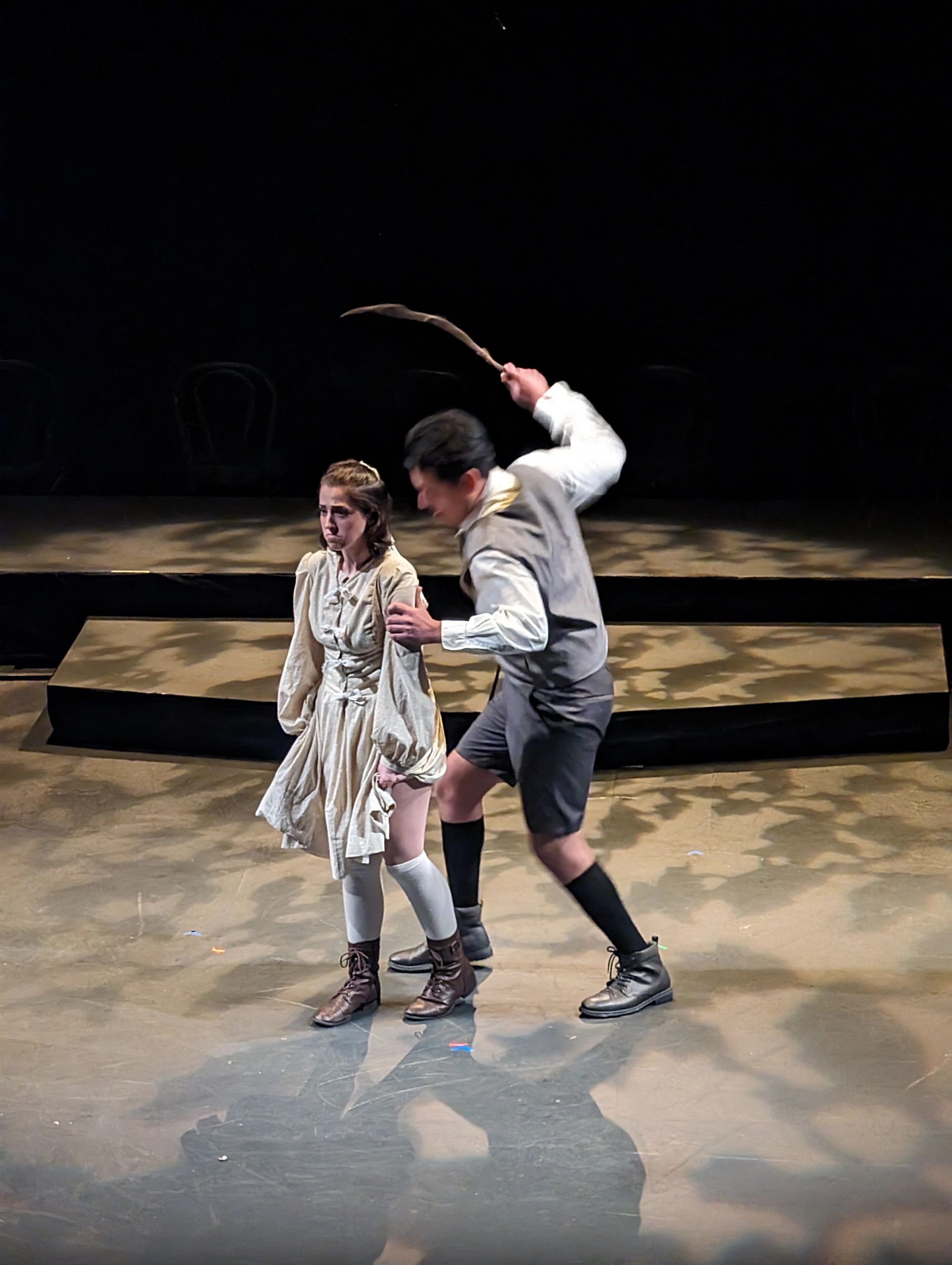 A man raising a stick to hit a sad woman in a theatrical scene.