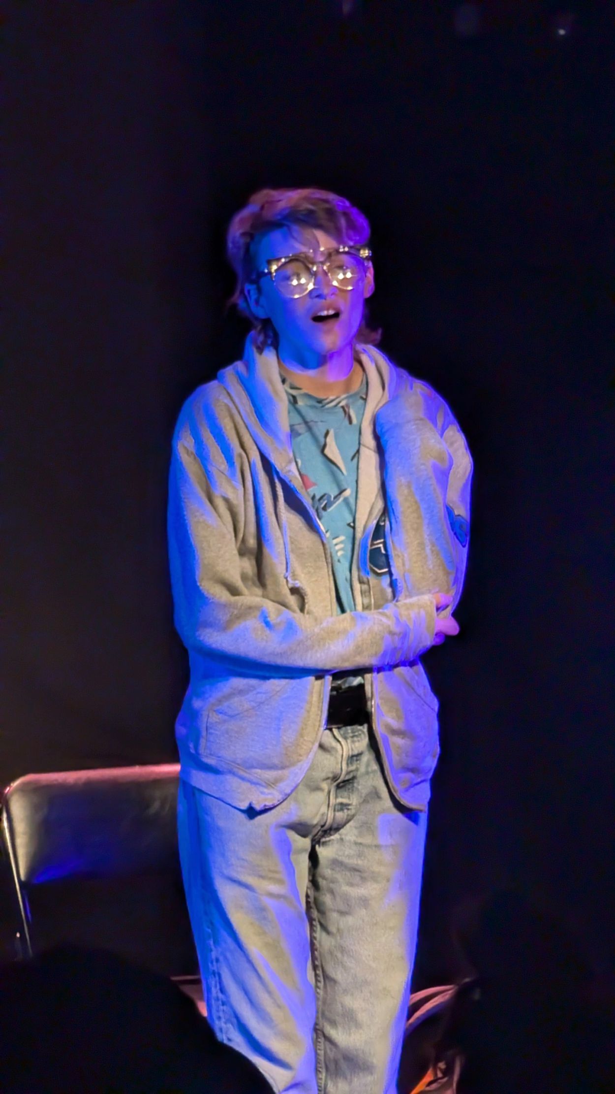 Person in illuminated glasses and casual clothing on stage.