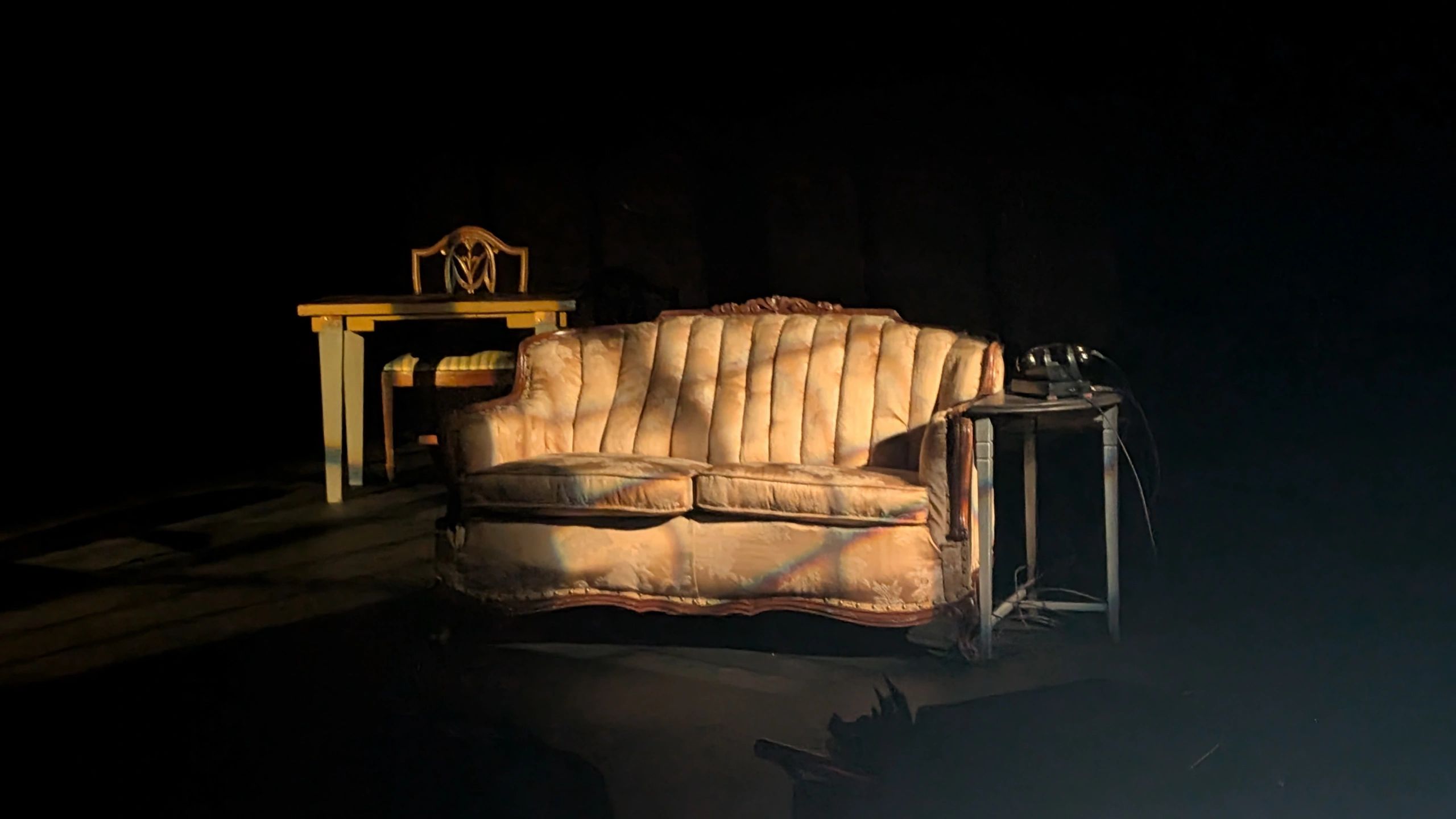 Vintage sofa, chair, table, and old phone in dim light.