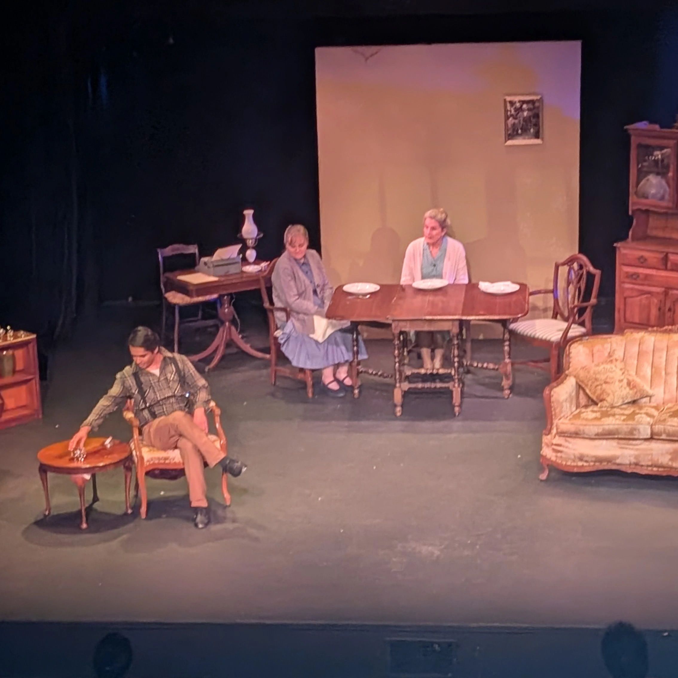 Actors on stage in a vintage living room set.