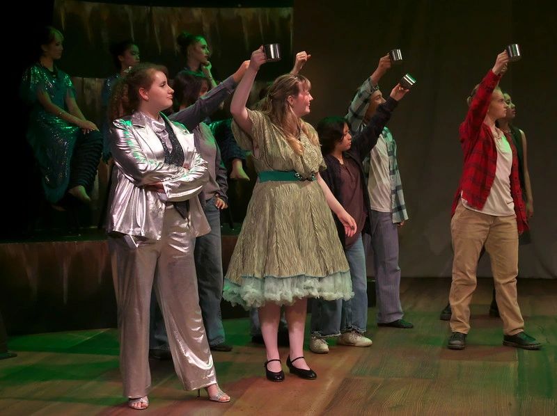 Actors on stage holding up mugs during a theatrical performance.