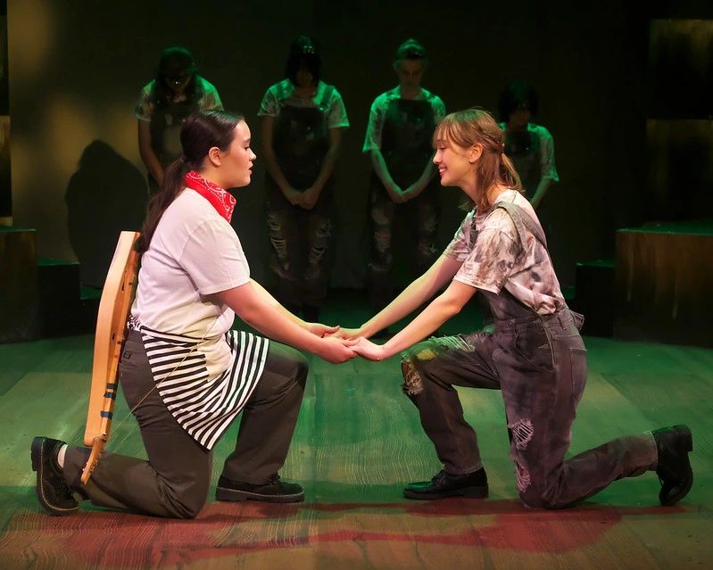 Two actors kneeling and holding hands in a theatrical performance.