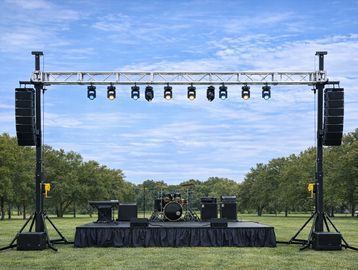 Empty outdoor stage setup with speakers and lighting on a grassy field.