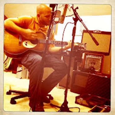 Man playing acoustic guitar in a recording studio.