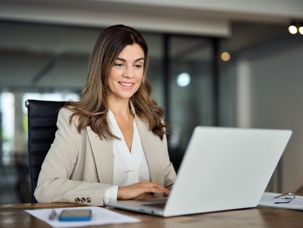 Smiling busy mature professional business woman looking at laptop computer technology in office 