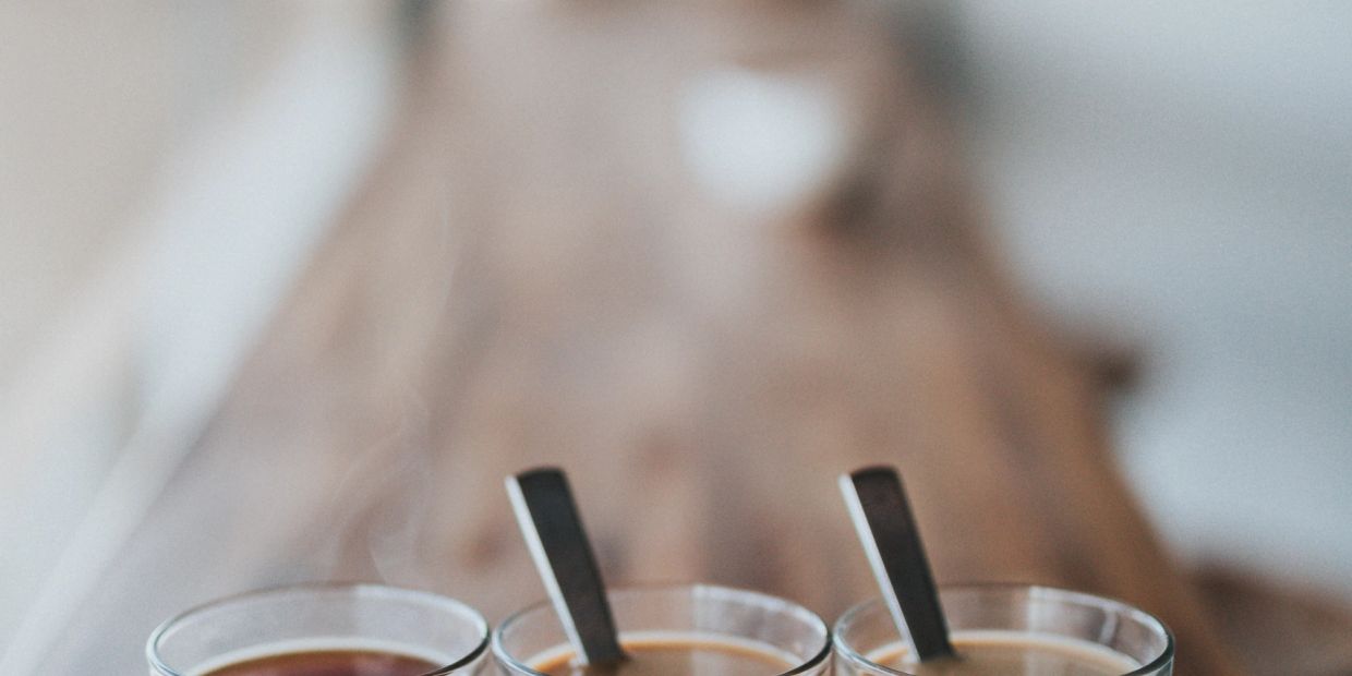 Three steaming cups of coffee with spoons on a wooden surface.