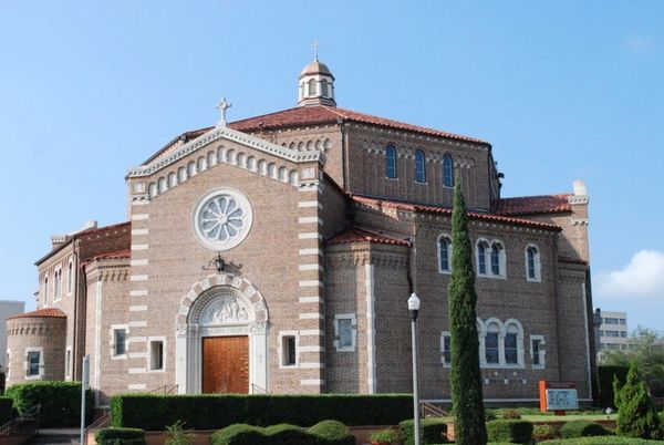 Historic brick church with a round window and red tile roof under a clear blue sky.