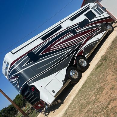 A large, modern RV with stylish black, white, and maroon graphics parked on a driveway.