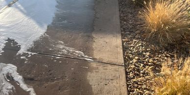 Sunlit sidewalk with melting snow and dry grass beside it.