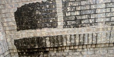 A brick wall with two sections of dark stains and one cleaned section.