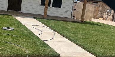 Newly laid concrete pathway through a green lawn in a residential backyard.