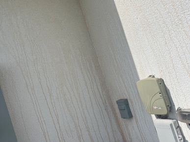 Water stains streak down a textured beige wall near outdoor utility boxes.