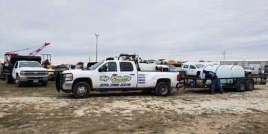 A white service truck parked on a dirt lot with a man working near a trailer.