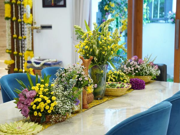Colorful floral arrangements decorate a dining table with blue chairs.