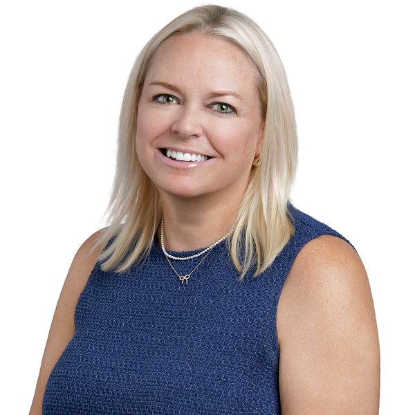 Professional headshot of Kayla smiling in her navy blue sleeveless dress.