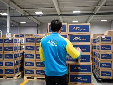 Worker organizing ABC Express packages in a warehouse.