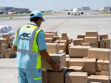 Worker handling packages at an airport with a plane in the background.
