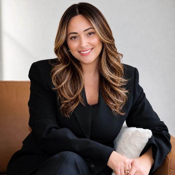 Woman in black suit sitting and smiling.