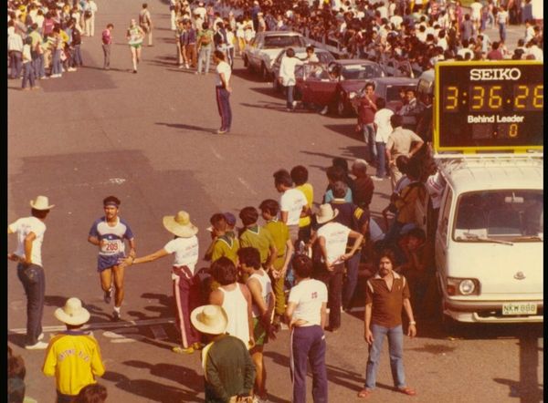 Runner nearing finish line in a crowded marathon event with timer display.
