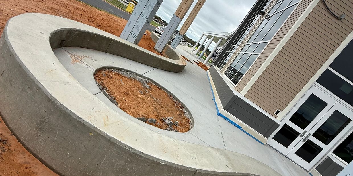 Curved concrete bench with a dirt planter in front of a modern building under construction.