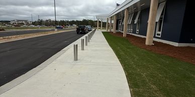 Sidewalk next to a building with bollards and parked cars under a cloudy sky.