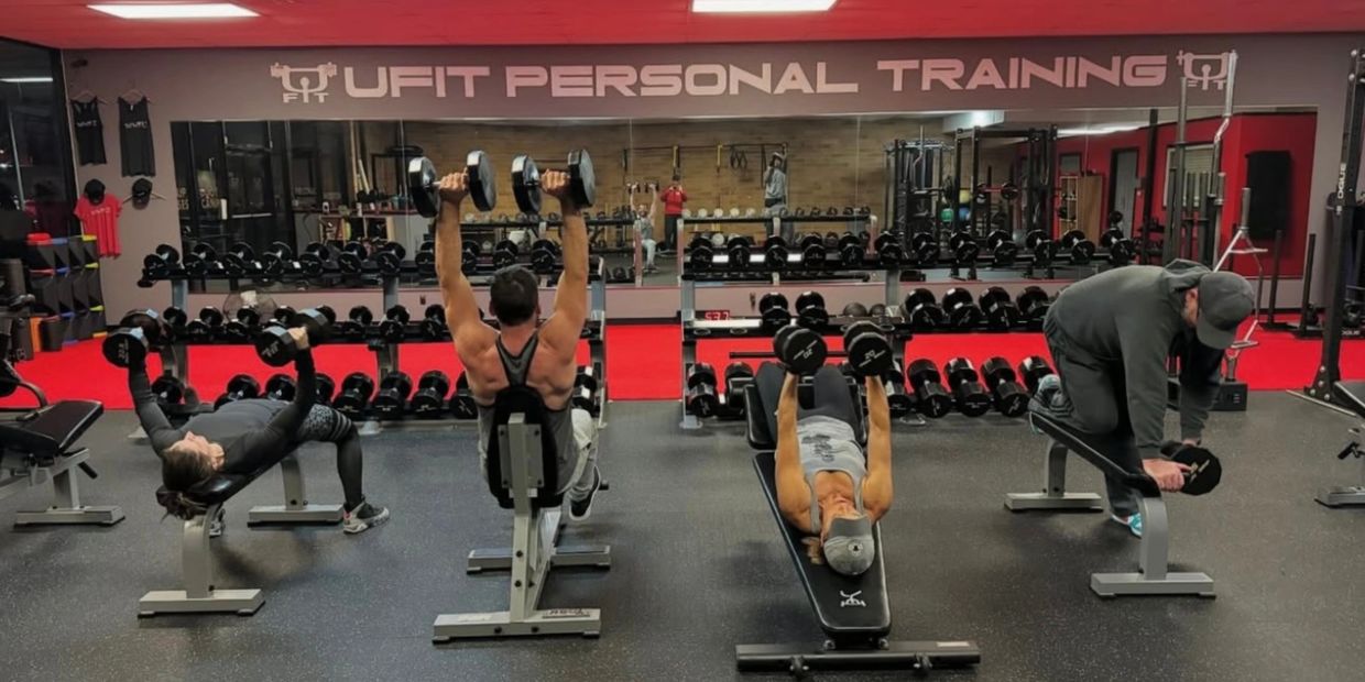 Four people doing dumbbell exercises on benches in a gym.