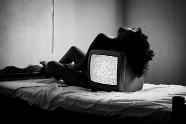 Pessoa deitada na cama com uma televisão antiga.
