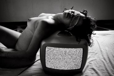 Pessoa deitada com os olhos vendados em cima de uma televisão antiga.