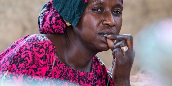Woman in pink headscarf thoughtfully biting her finger.